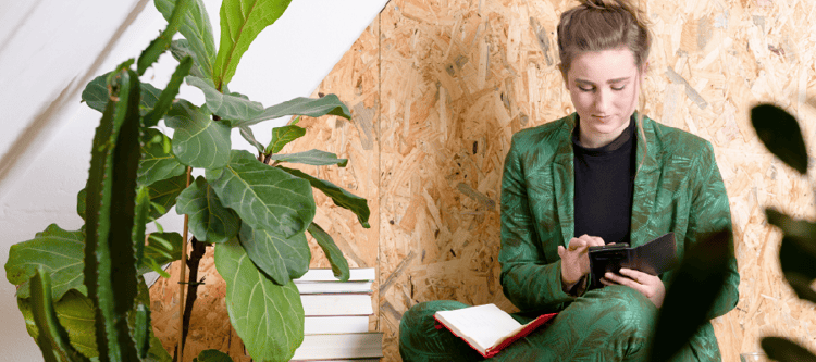 Mulher em um traje verde analisando informações em um tablet, rodeada por plantas e um ambiente moderno. Ideal para temas de trabalho e bem-estar.